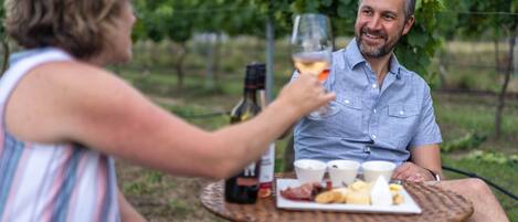 Two people sitting at an outdoor table with a bottle of wine, glasses, and a plate of food.
