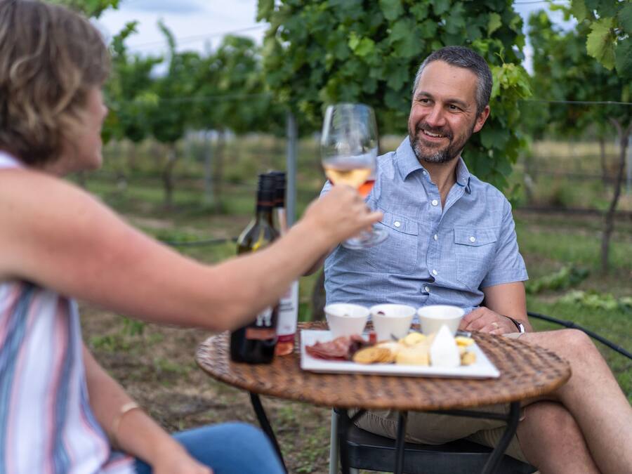 Two people sitting at an outdoor table with a bottle of wine, glasses, and a plate of food.