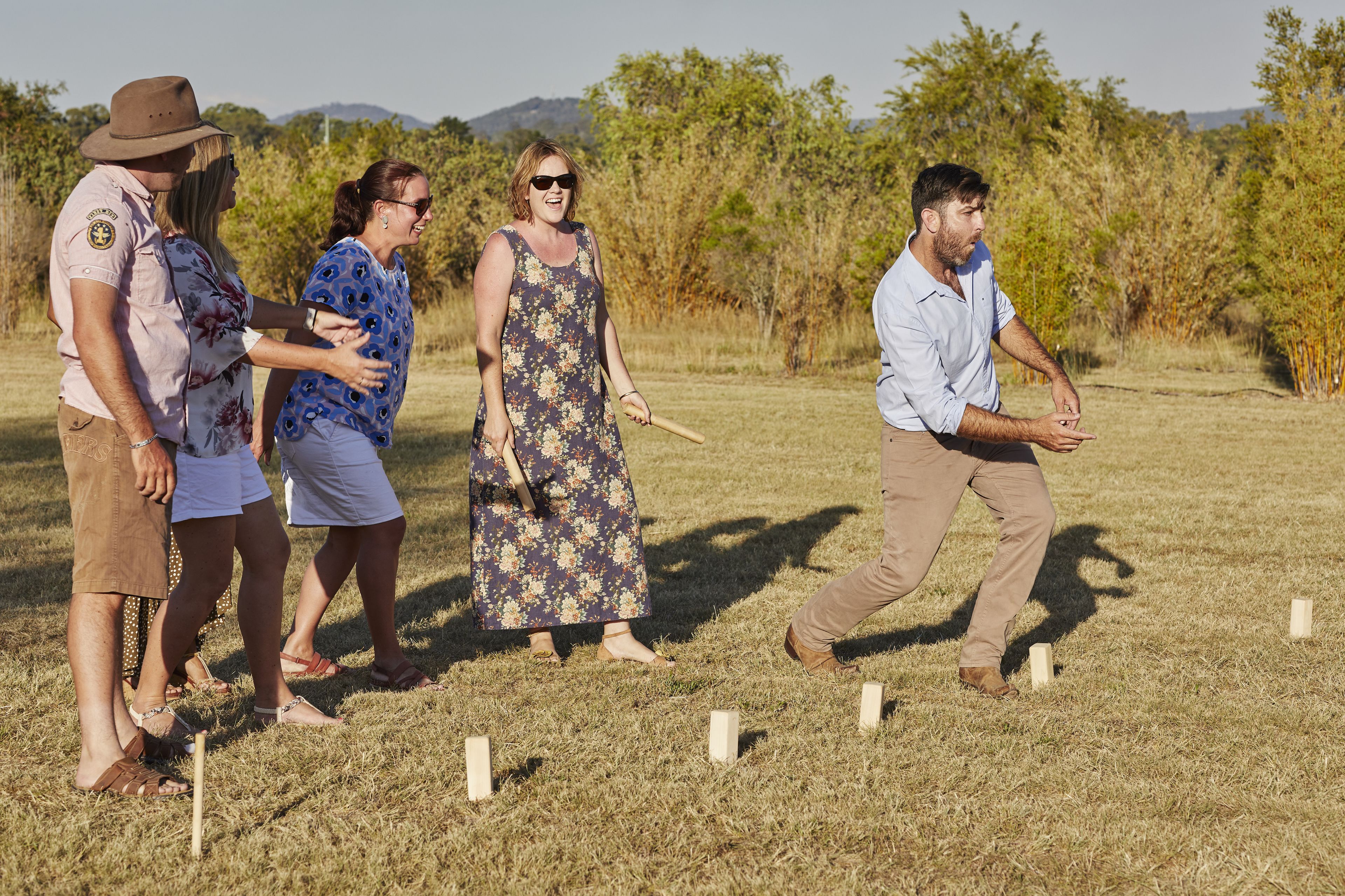 A group of people playing a game in an open field with trees and hills in the background.