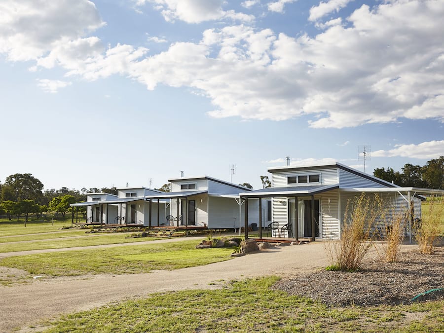 A row of single-story mobile homes with attached porches, set in a grassy area with a clear sky.