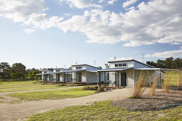 A row of single-story mobile homes with attached porches, set in a grassy area with a clear sky.