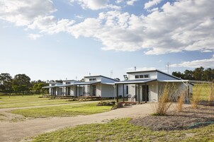 A row of single-story mobile homes with attached porches, set in a grassy area with a clear sky.