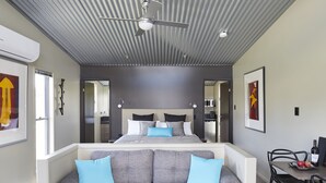 A modern bedroom with a large bed, a ceiling fan, a dining area with a table and chairs, and a sofa with blue cushions. - Ridgemill Escape (Broadwater)