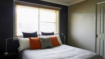 A bedroom with a bed, a nightstand, a lamp, and a window with blinds.