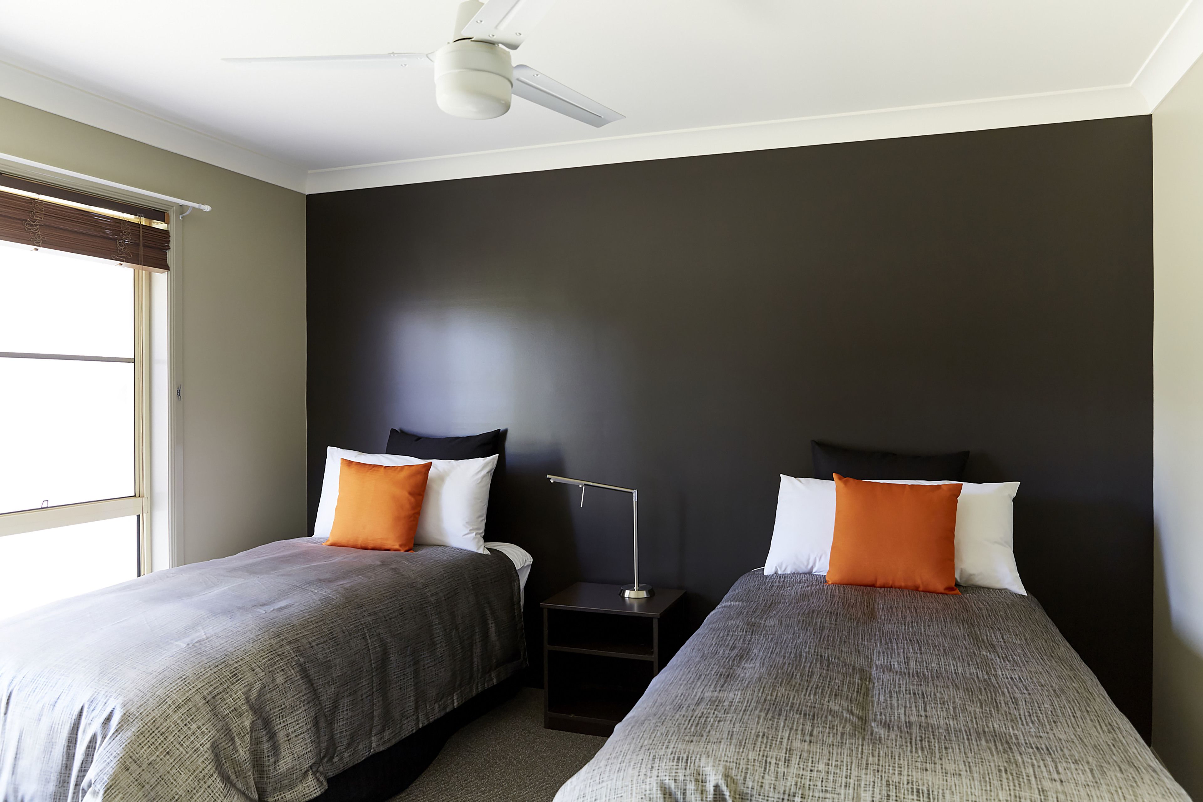 A bedroom with two beds, a nightstand, a ceiling fan, and a window with blinds.