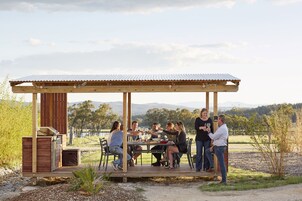 A wooden outdoor dining area with a metal roof, surrounded by natural landscape.