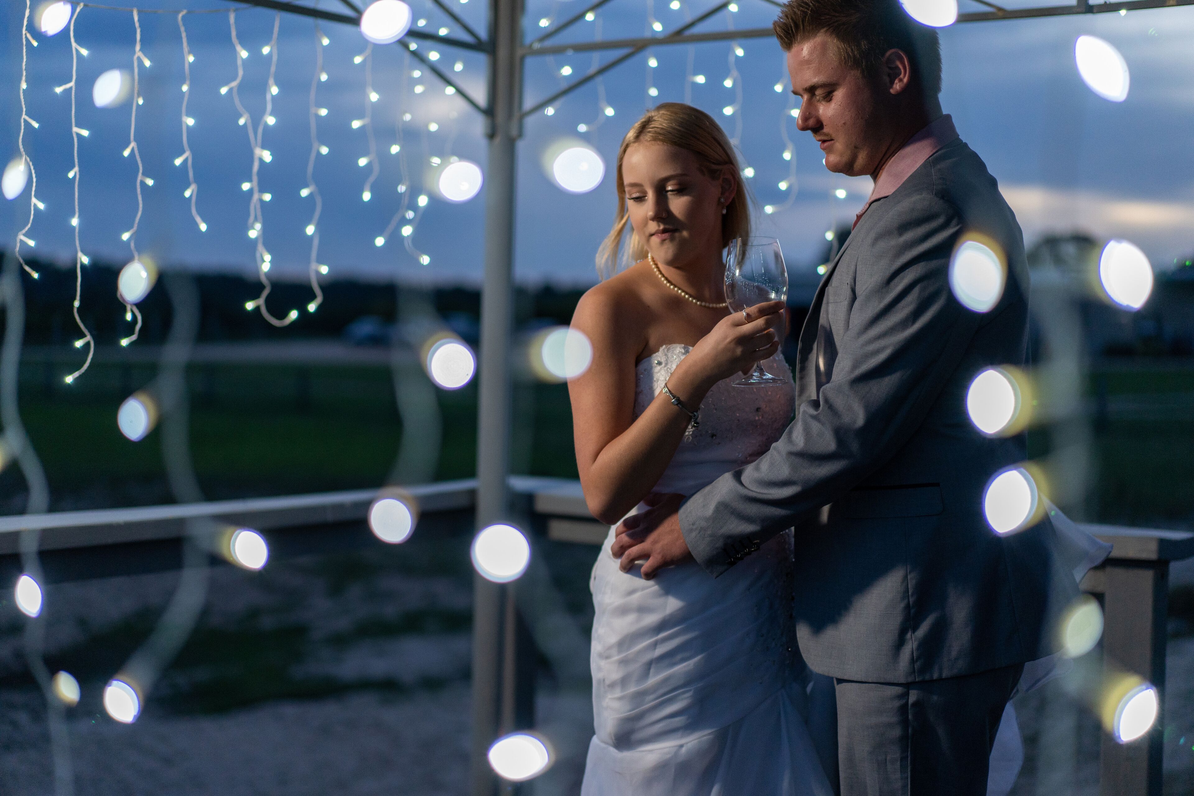 A couple embracing under string lights, with a clear sky in the background.
