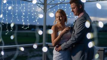 A couple embracing under string lights, with a clear sky in the background.