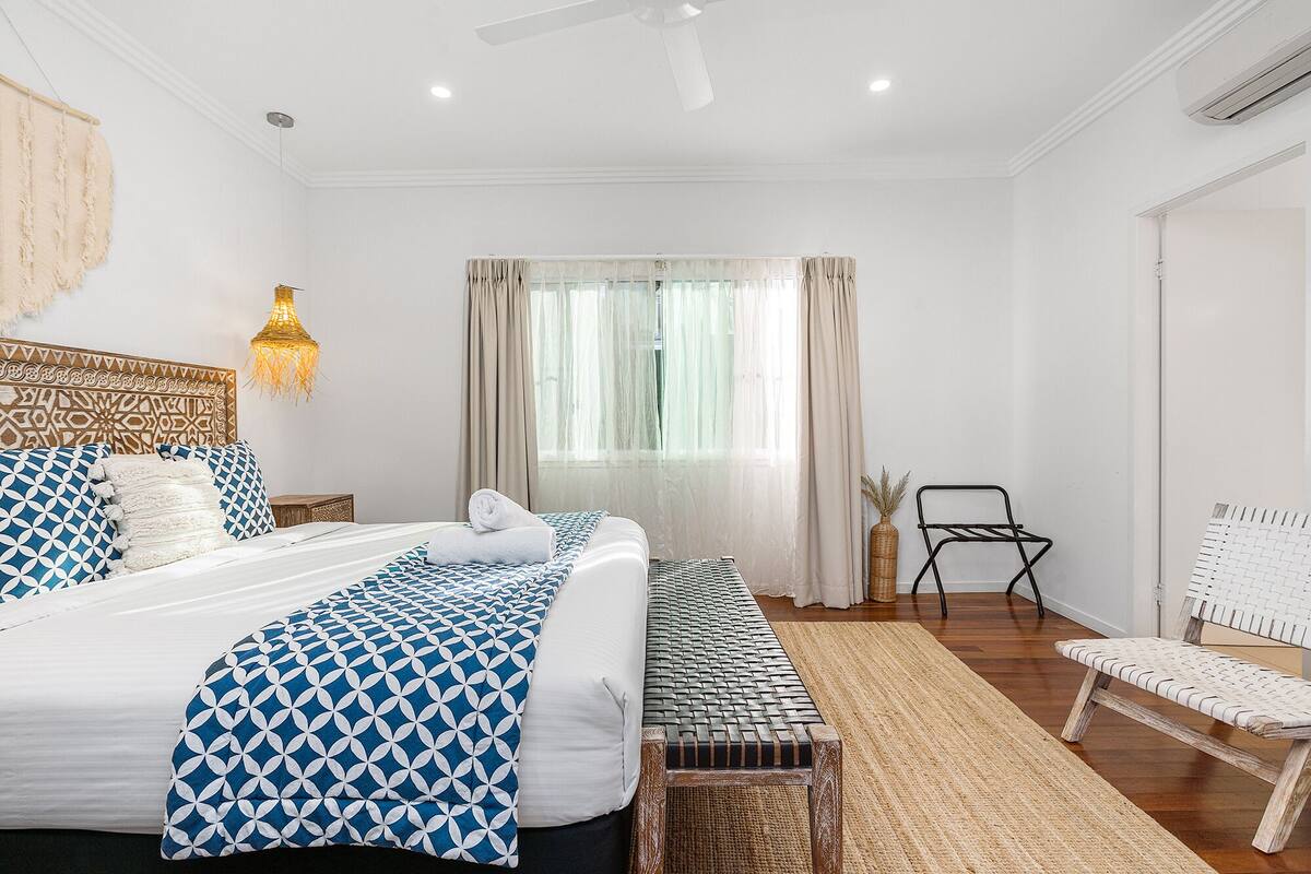 A bedroom with a large bed, a bench, a chair, and a ceiling fan.
