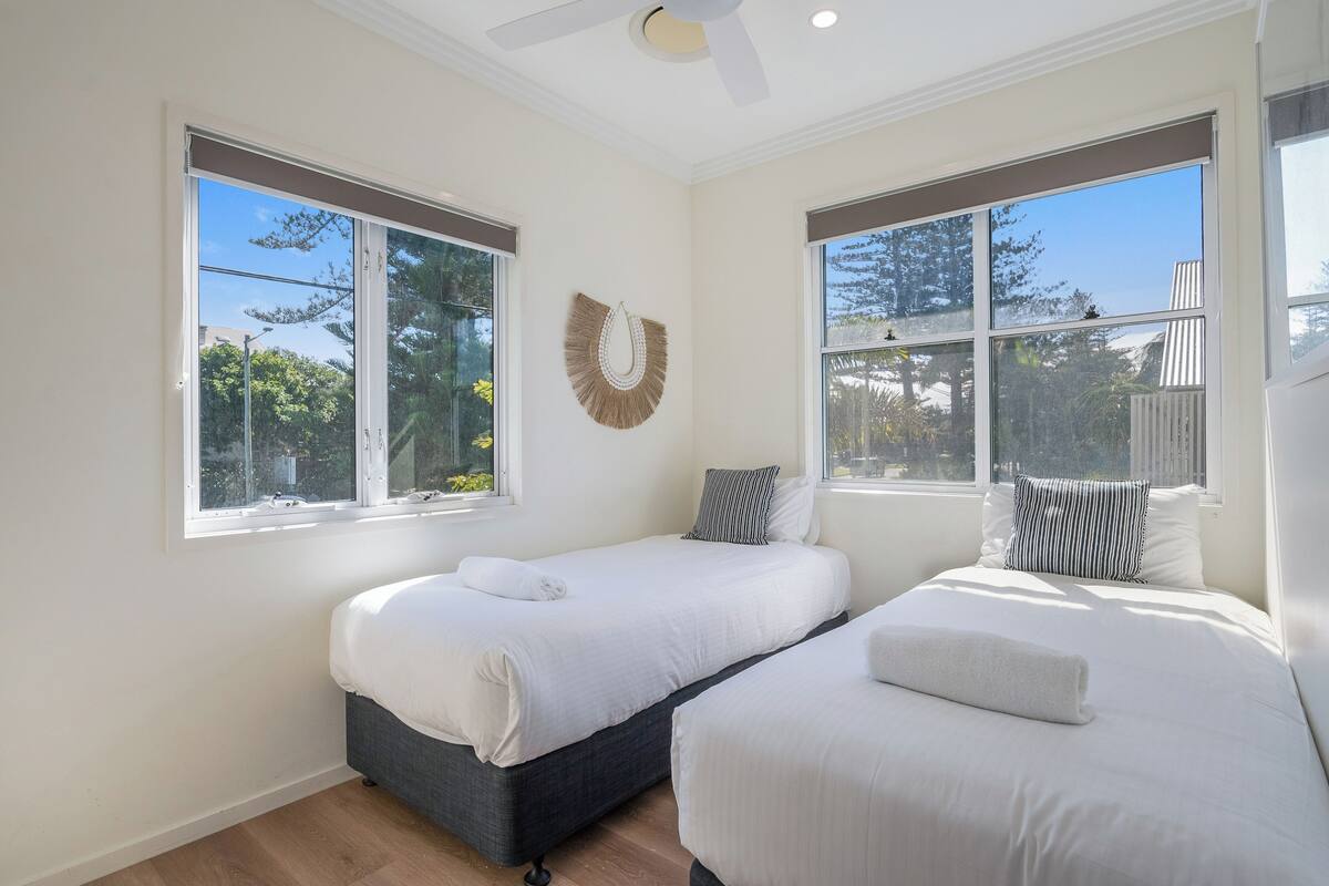 A room with two beds, large windows, and a ceiling fan.