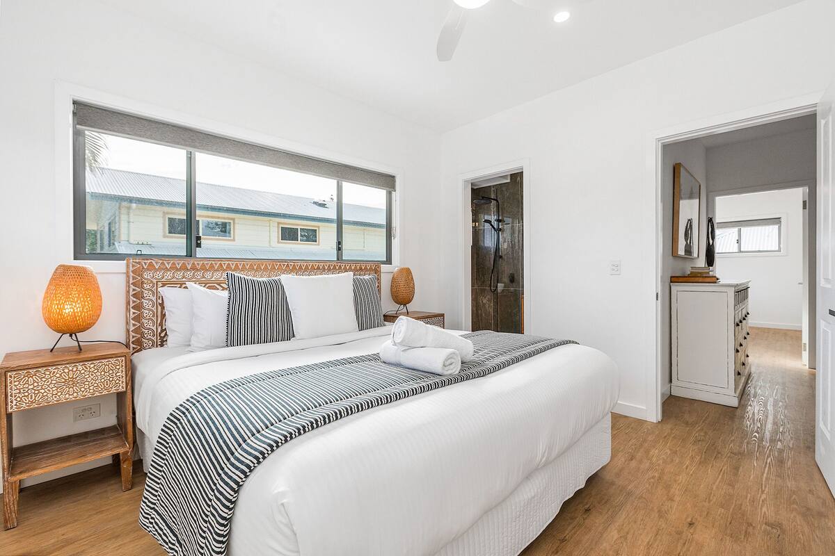 A hotel room with a large bed, a bedside table with a lamp, a shower area, and a view of the outside.