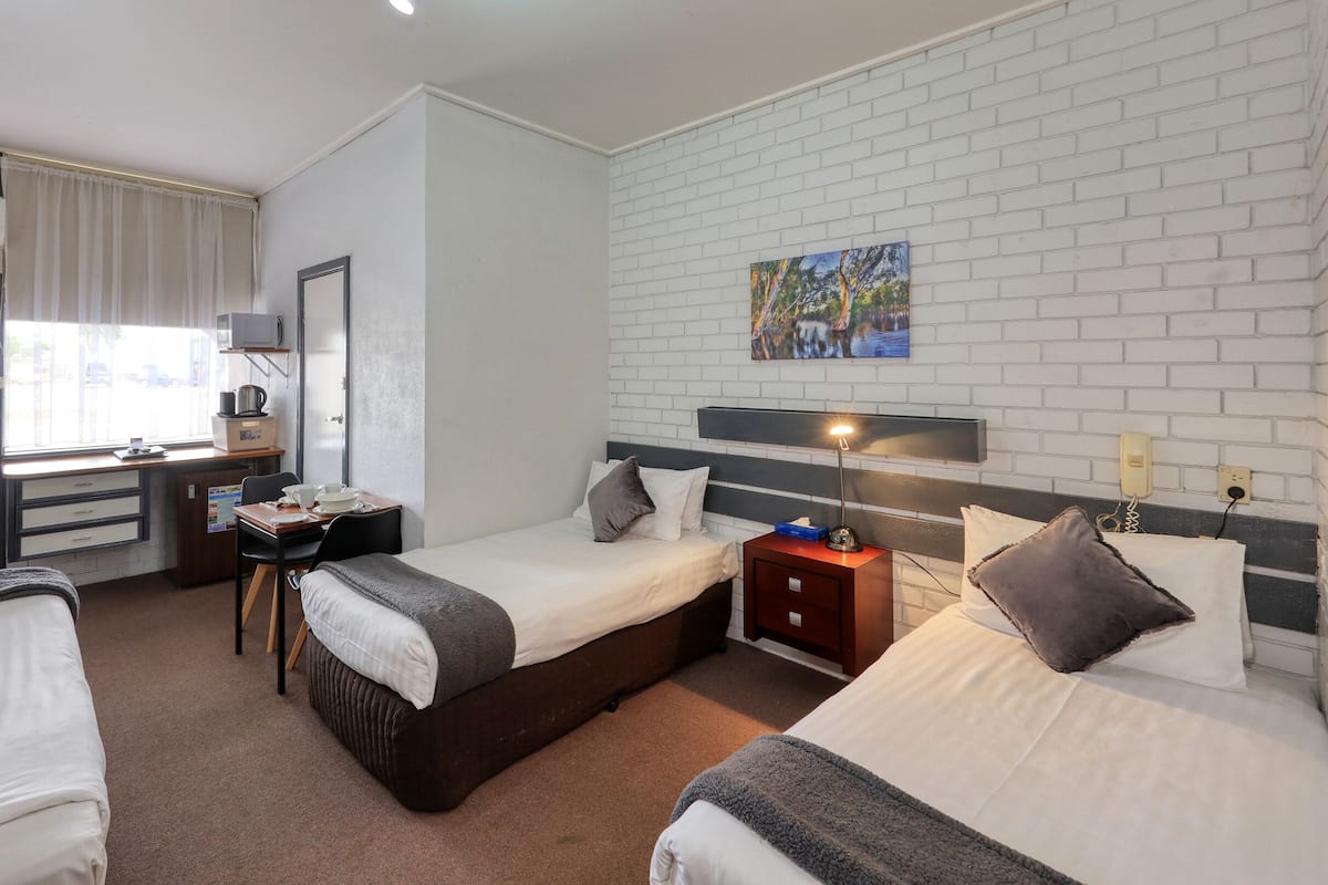 A hotel room with two beds, a desk, a chair, a microwave, a small refrigerator, and a painting on the wall.
