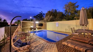 A backyard with a swimming pool, lounge chairs, a TV, and a wooden fence. - Sun Centre Motel (Swan Hill)