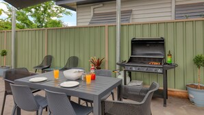 An outdoor patio with a grill, dining table, chairs, and potted plants. - Sun Centre Motel (Swan Hill)