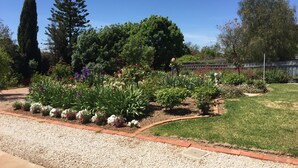 A well-maintained garden with a variety of flowers and trees, a clear sky, and a paved walkway. - Lyreen's Apartment B&B (Auburn)