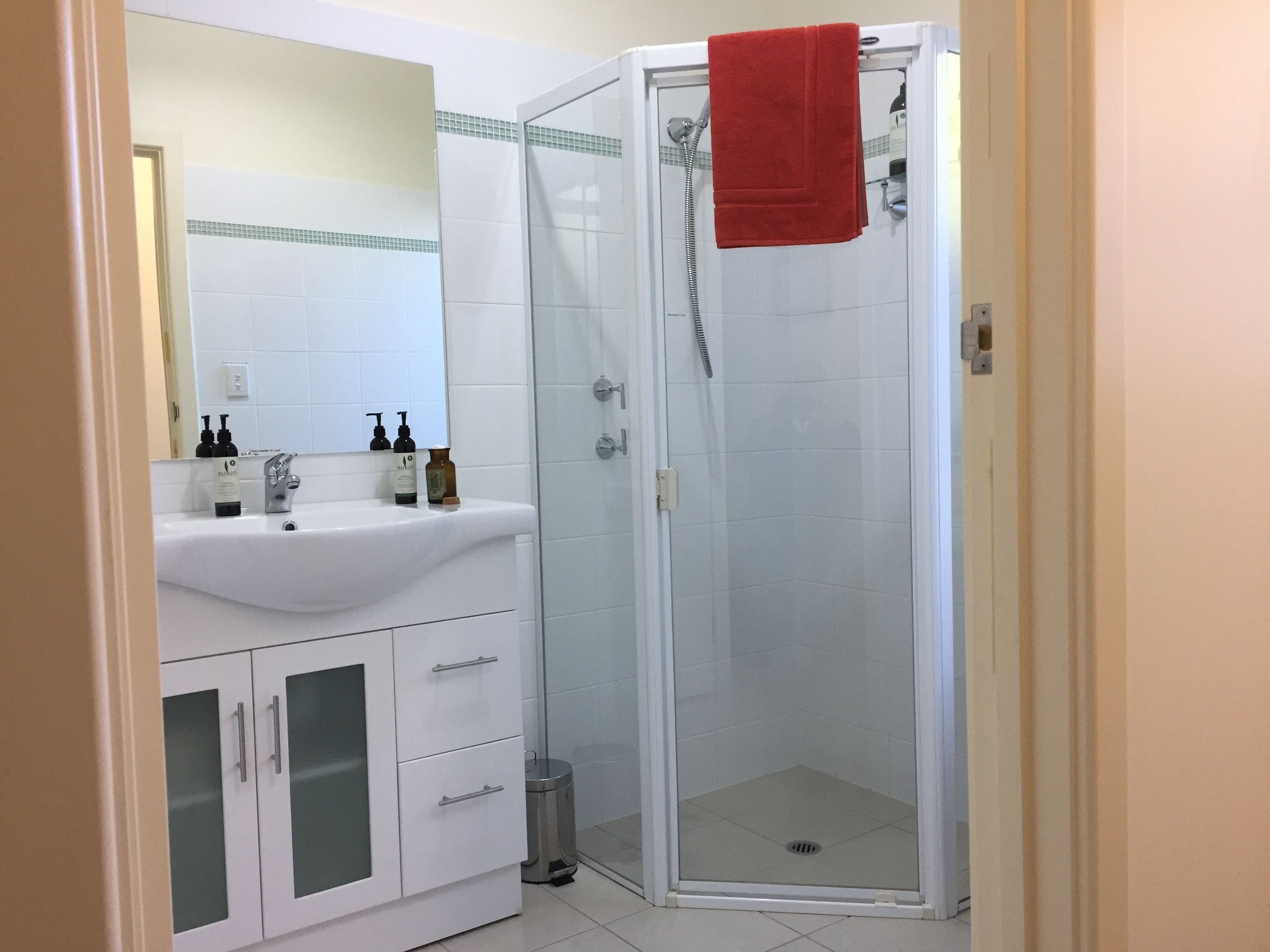 Een badkamer met een wit wastafelmeubel, spiegel en een douchecabine van glas.
