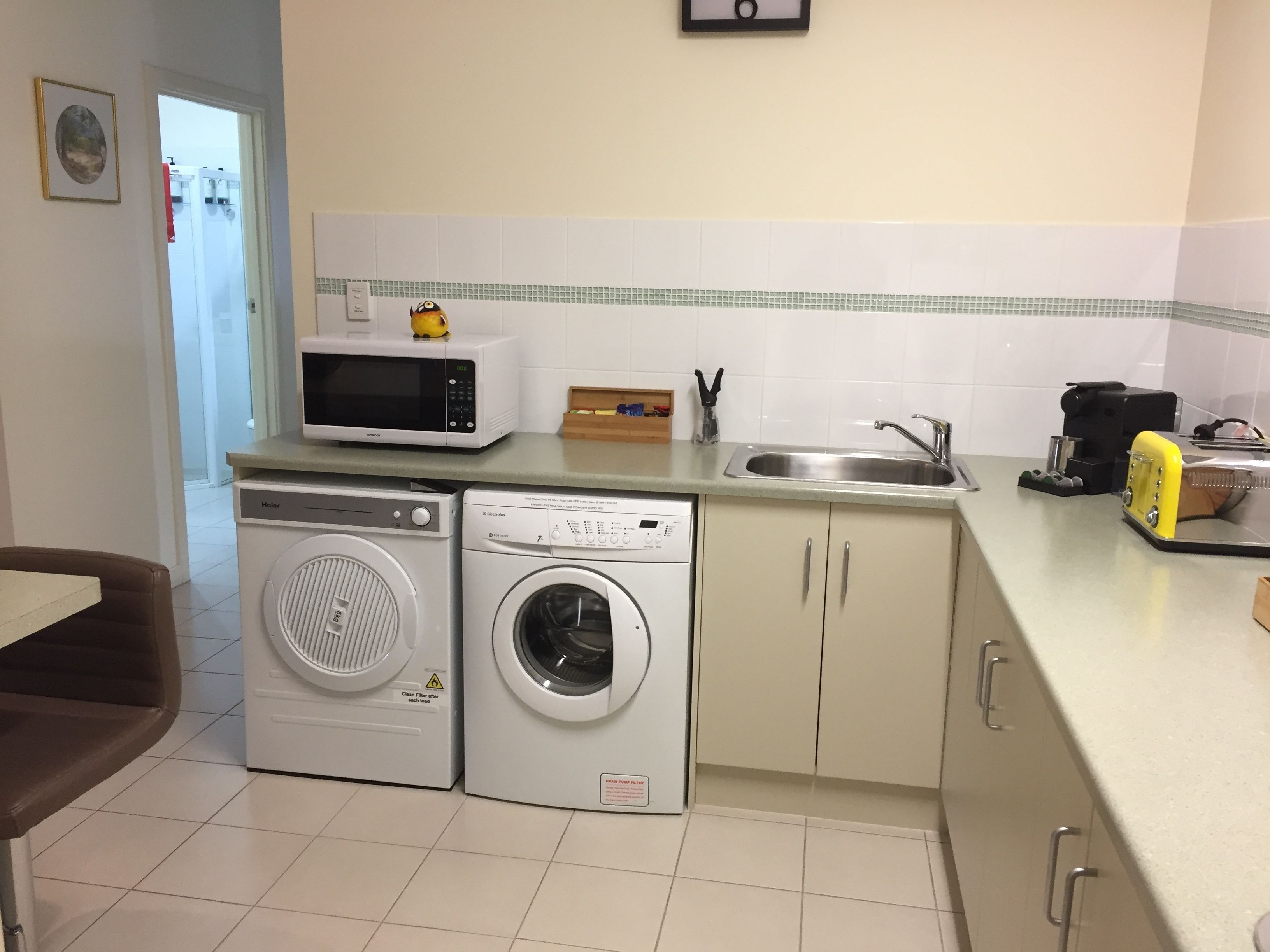 A compact kitchen with a microwave, washing machine, and sink.