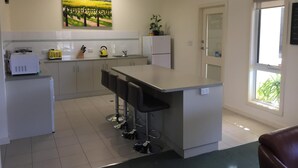 A modern kitchen with a central island, bar stools, a refrigerator, and a painting of a vineyard. - Lyreen's Apartment B&B (Auburn)