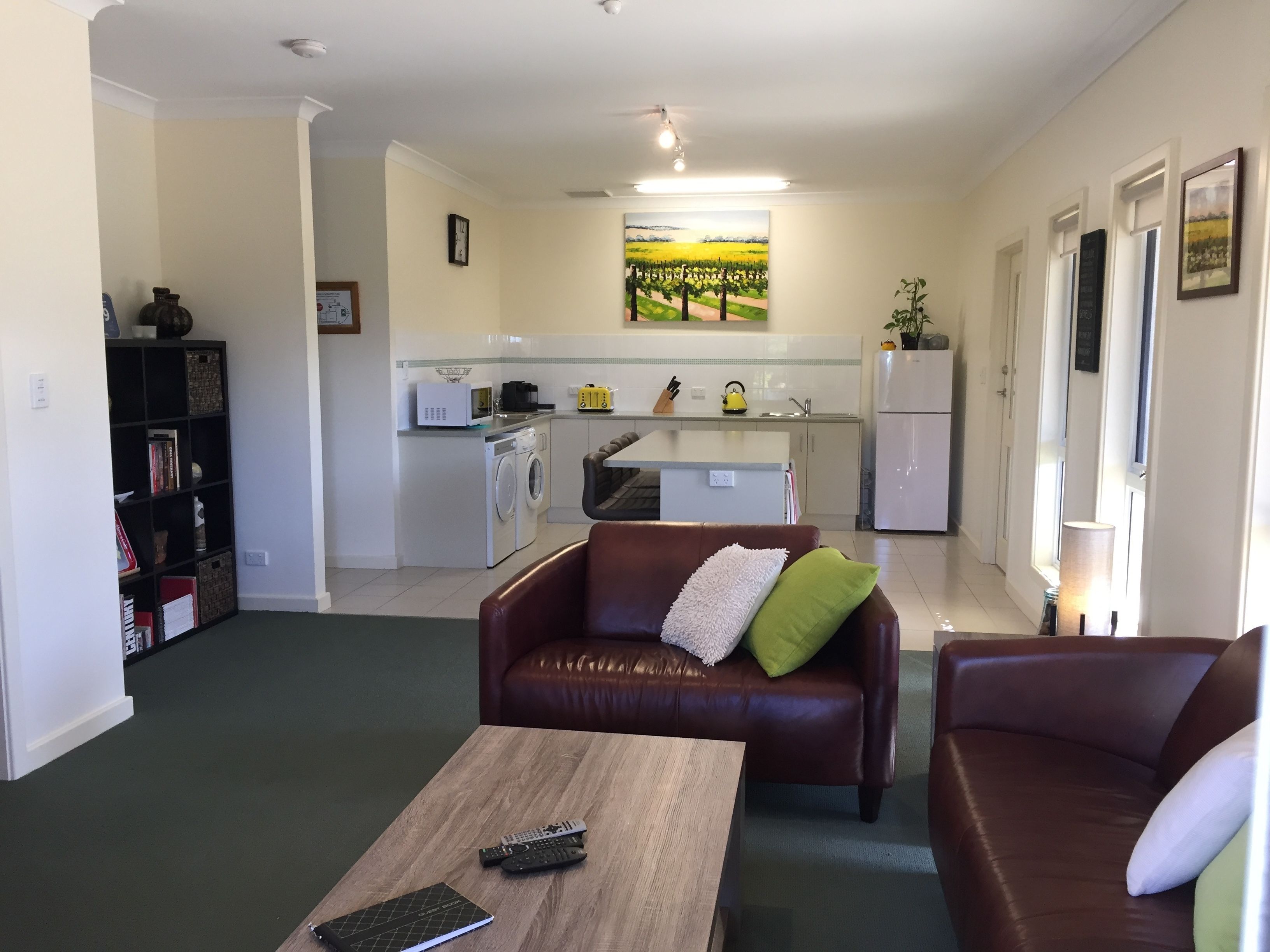 Un espacio habitable pequeño con kitchenette, un sofá de cuero marrón, una mesa de centro de madera y una estantería.