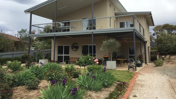 A two-story house with a balcony, a garden with various plants and flowers, and a driveway. - Lyreen's Apartment B&B (Auburn)