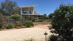 A two-story house with a balcony, surrounded by a garden with various plants and a gravel driveway. - Lyreen's Apartment B&B (Auburn)