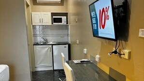 Ein kompaktes Hotelzimmer mit Küchenzeile, einem Bett, einem Esstisch und einem Fernseher, der eine Anzeige mit 10% Rabatt zeigt.