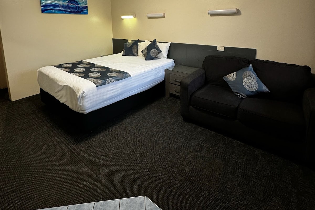 A hotel room with a bed, a black couch, a small table, and a ceiling light.