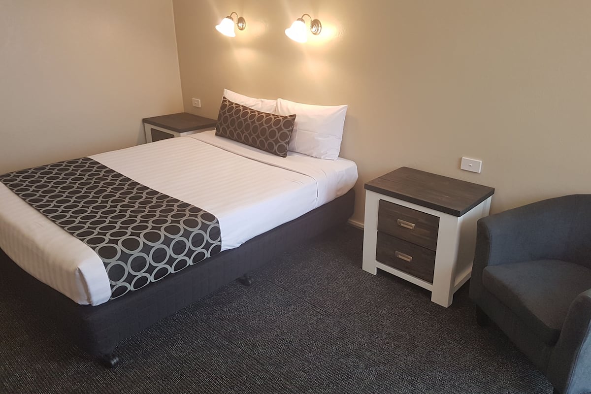 A neatly arranged hotel room with a bed, two bedside tables, a chair, and wall-mounted lights.
