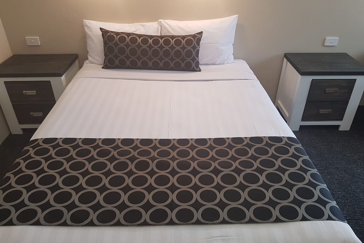A neatly made bed with a patterned throw, white pillows, and two bedside tables with drawers.