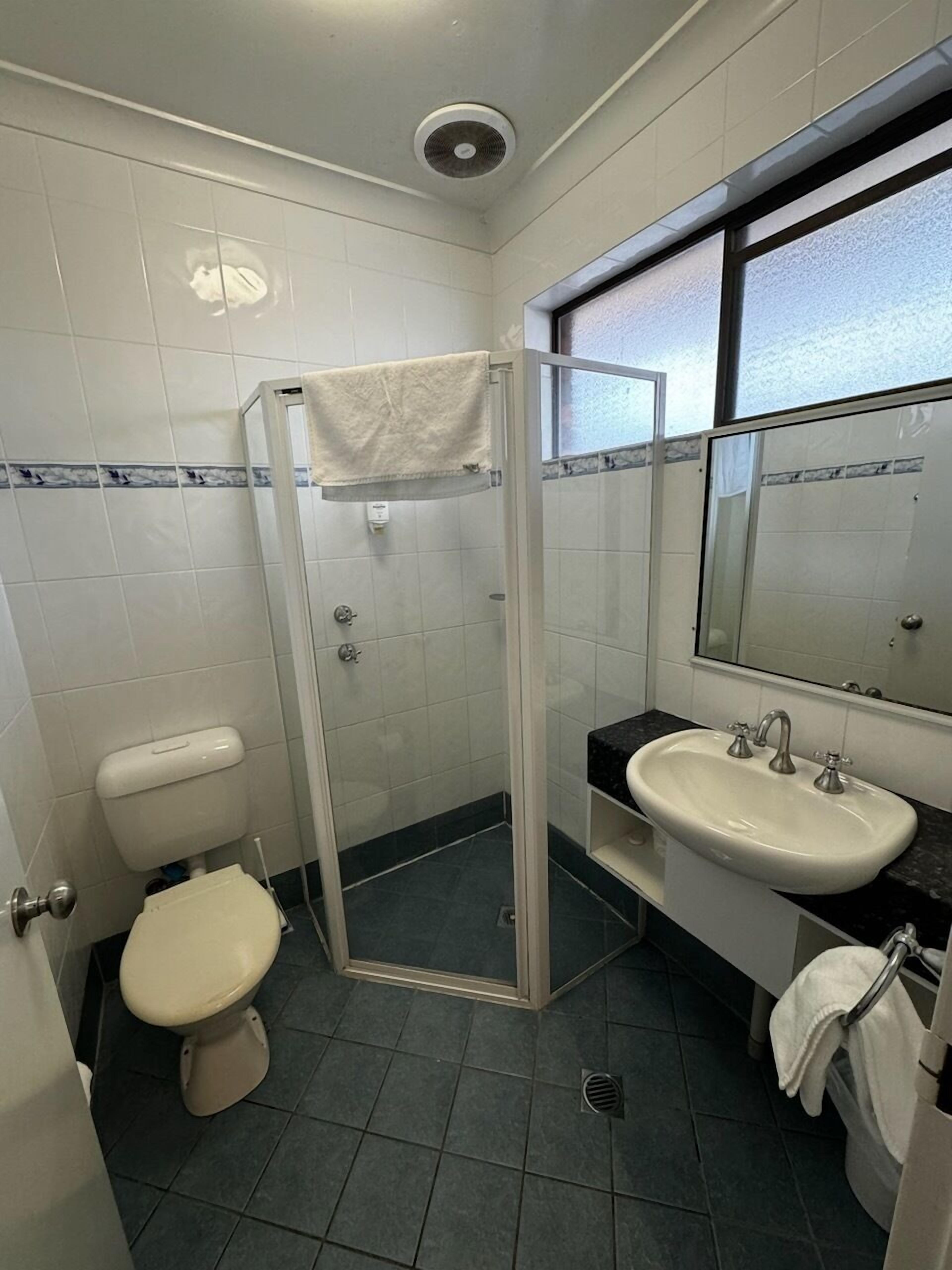 A bathroom with a toilet, a glass shower enclosure, a sink, and a mirror.
