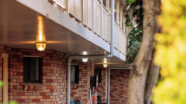 A building with a brick facade, outdoor seating, and a tree in the foreground. - Scone Motor Inn (Scone)