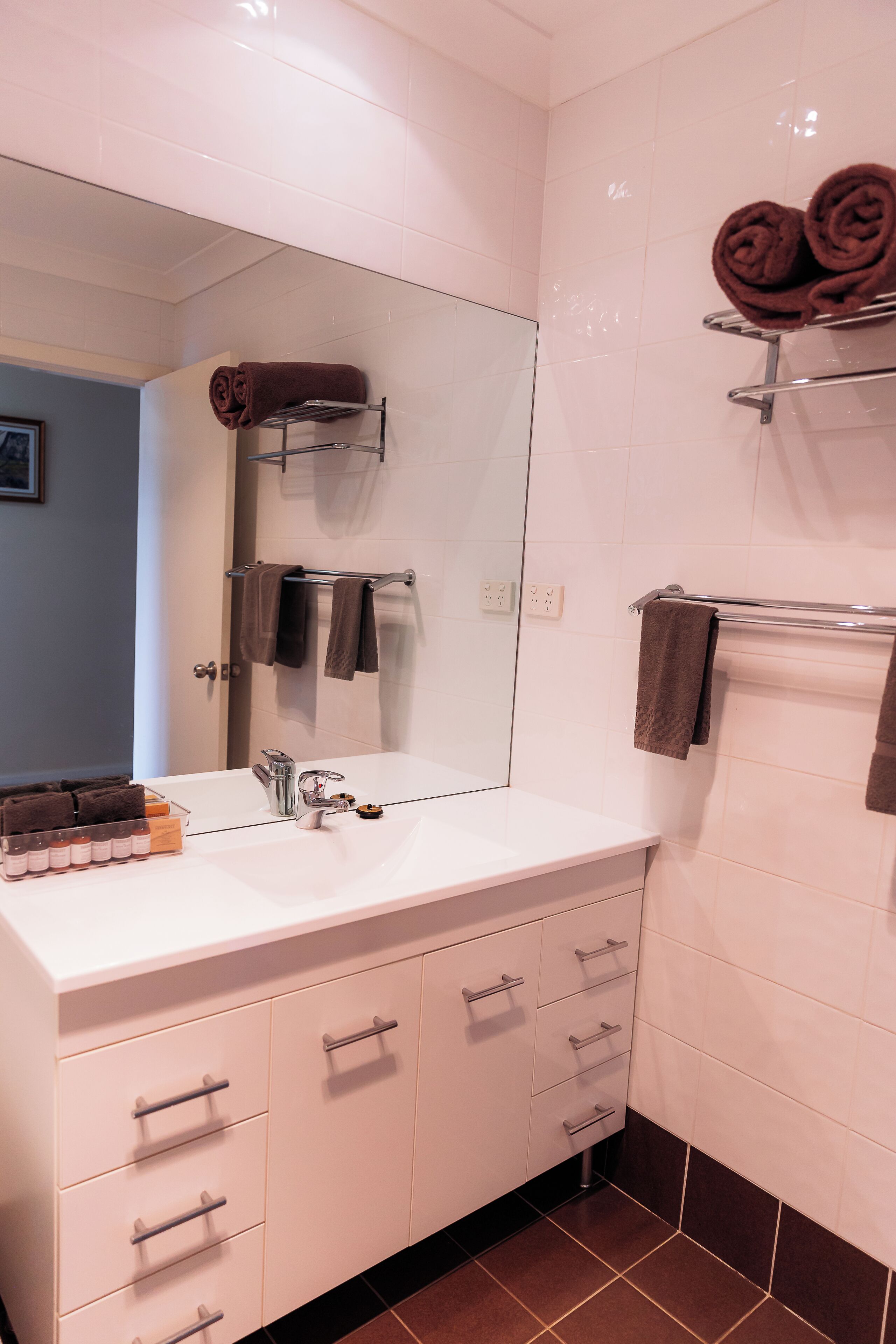 Une salle de bain moderne avec un lavabo blanc, un miroir et un porte-serviettes sur lequel sont pliés des serviettes.