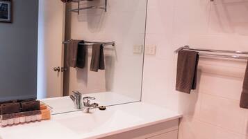Une salle de bain moderne avec un lavabo blanc, un miroir et un porte-serviettes sur lequel sont pliés des serviettes.