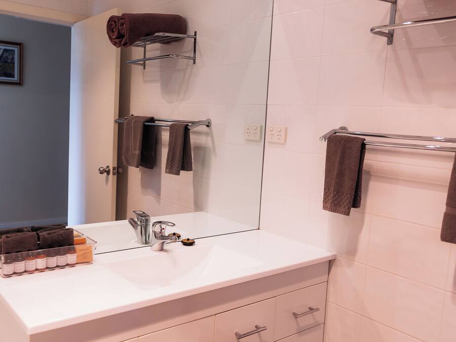 Une salle de bain moderne avec un lavabo blanc, un miroir et un porte-serviettes sur lequel sont pliés des serviettes.