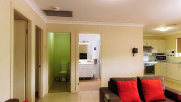 A living room with a brown sofa and red cushions, a kitchen with white cabinets and appliances, and a green bathroom.