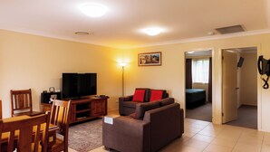 A living room with a sofa, TV, wooden chairs, and a dining table. - Scone Motor Inn (Scone)