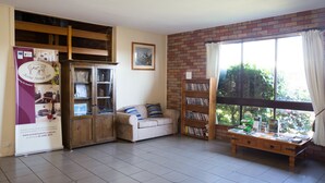 A room with a sofa, a wooden cabinet, a bookshelf, and a window with curtains. - Scone Motor Inn (Scone)