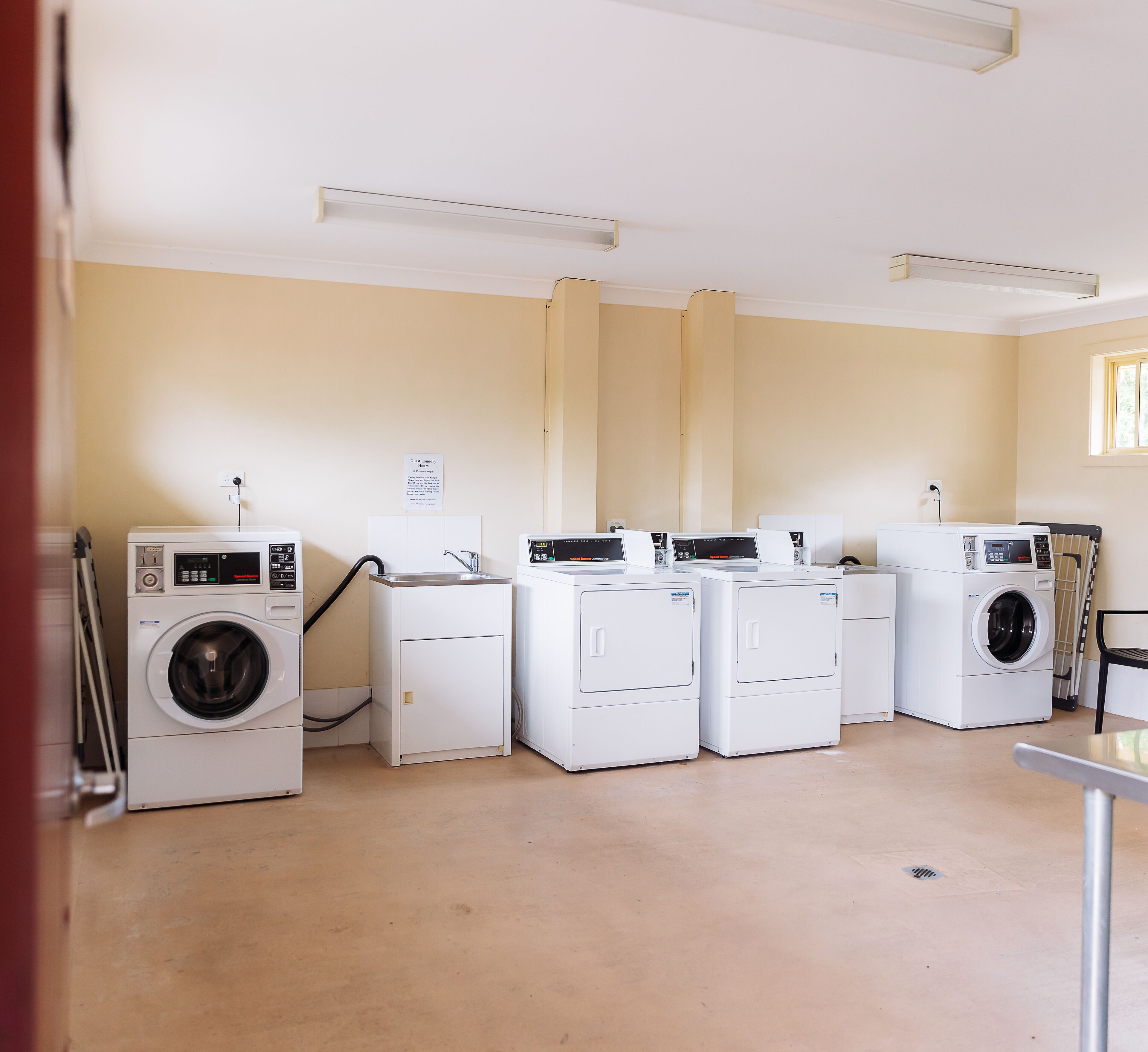 Une buanderie équipée de plusieurs machines à laver, d’un évier et d’un panneau indiquant qu’elle est réservée à l’usage des clients.