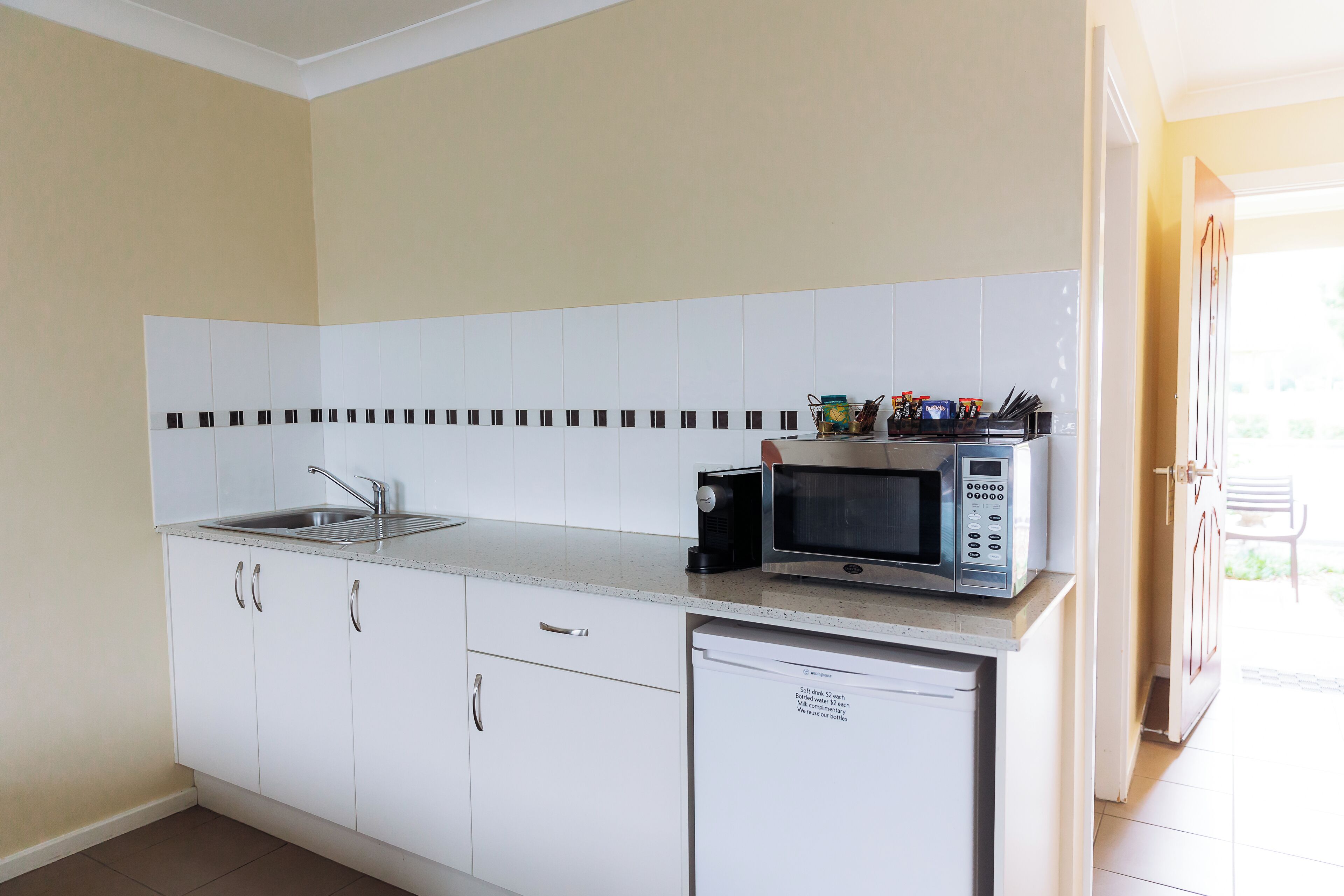 A kitchen with white cabinets, a stainless steel sink, a microwave, and a refrigerator.