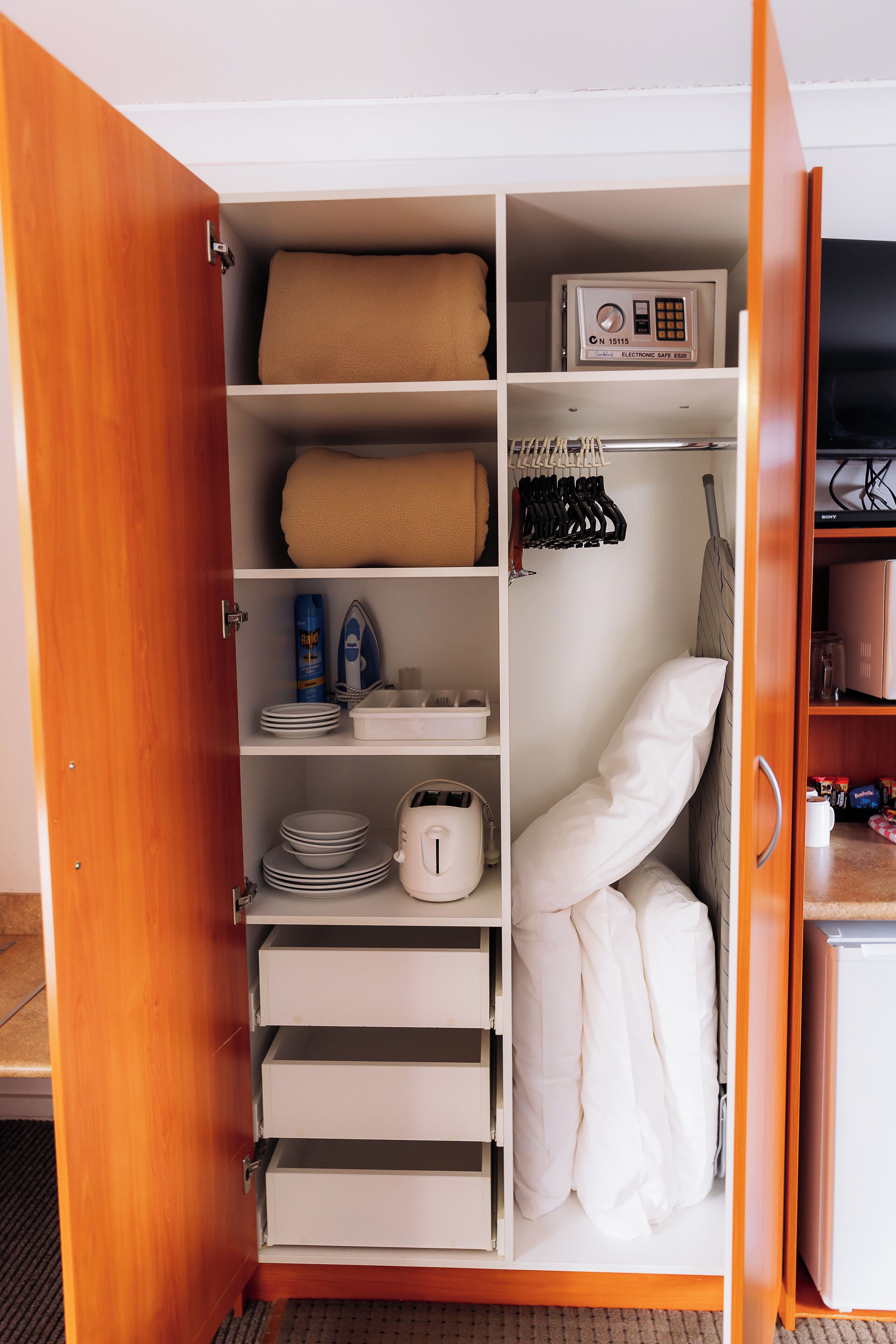 Ein Hotelkleiderschrank mit Regalen, einer Mikrowelle und einer Kleiderstange.