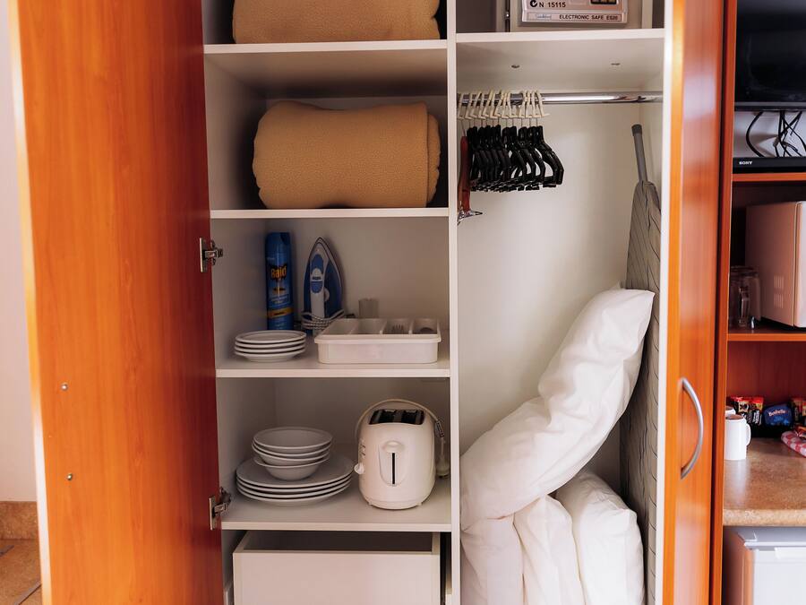 Ein Hotelkleiderschrank mit Regalen, einer Mikrowelle und einer Kleiderstange.