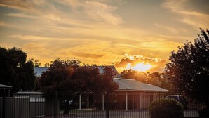 A fenced property with a building, trees, and a sunset. - Scone Motor Inn (Scone)