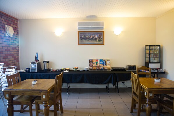 A dining area with a long table, chairs, a coffee station, and a framed picture on the wall.