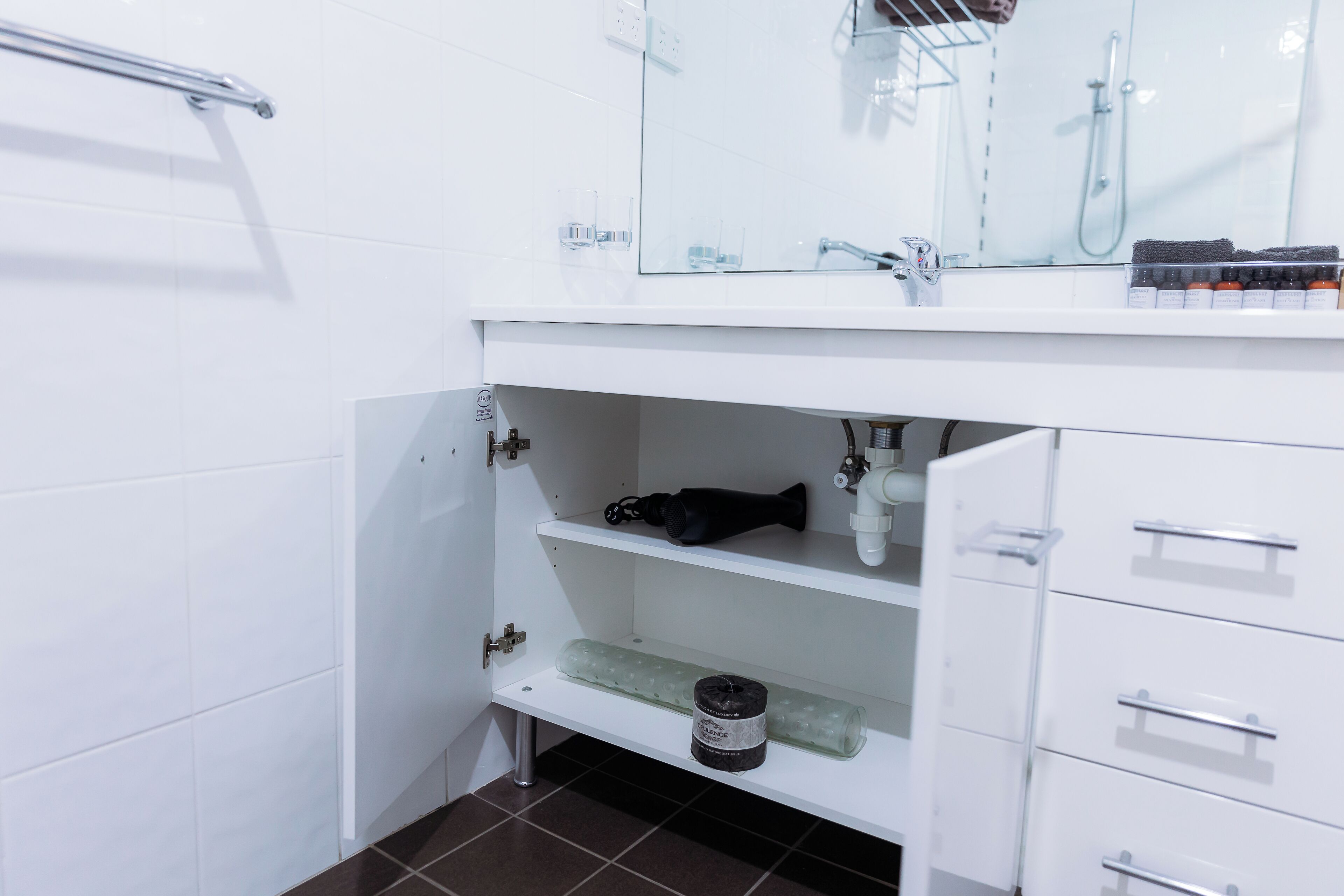 A bathroom with a white vanity, a mirror, a towel rack, and a shelf with toiletries.