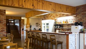 A bar area with wooden chairs and a counter, a refrigerator, and shelves with bottles. - Scone Motor Inn (Scone)