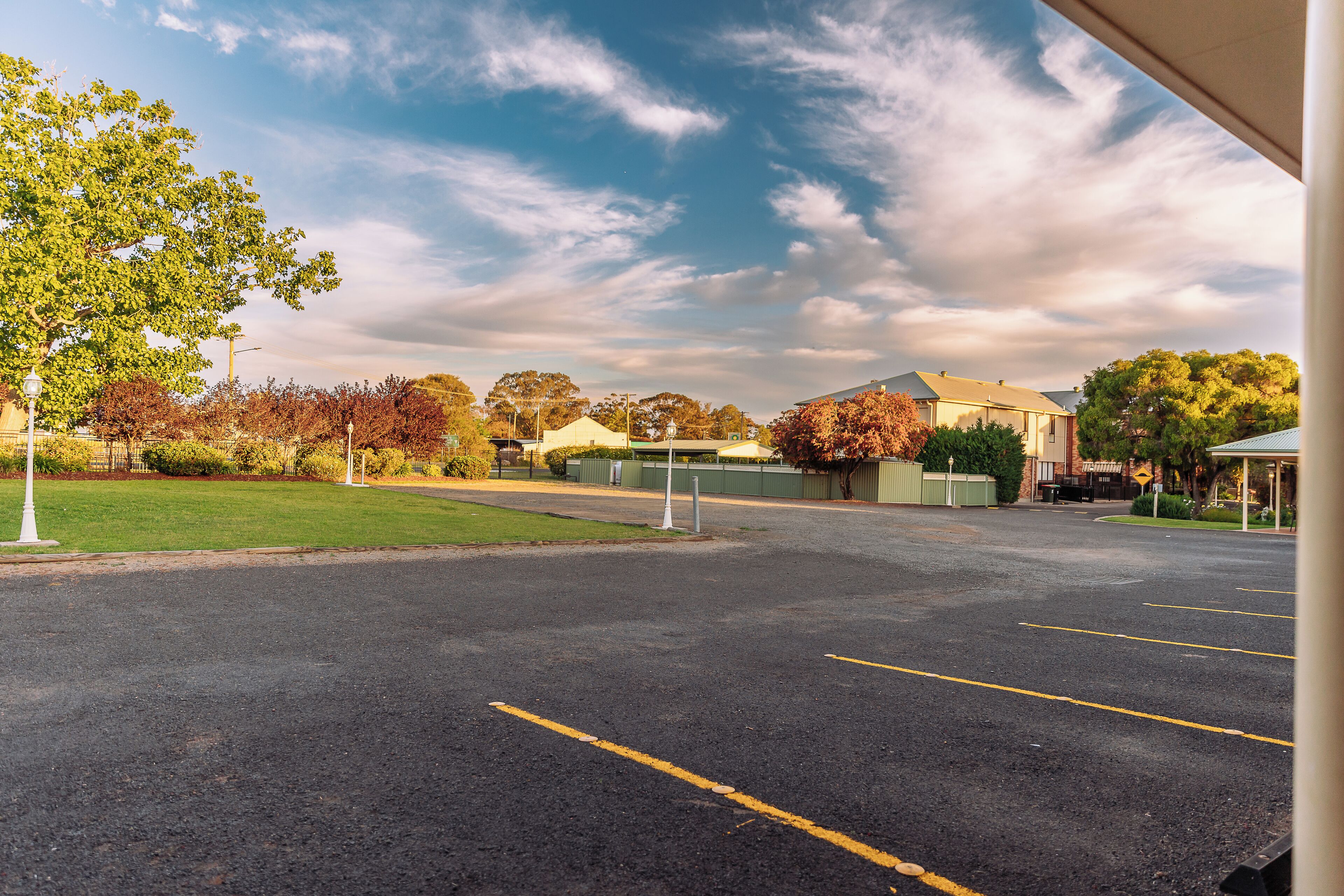 A parking lot with marked spaces, a green lawn, and buildings in the background.