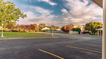 A parking lot with marked spaces, a green lawn, and buildings in the background.