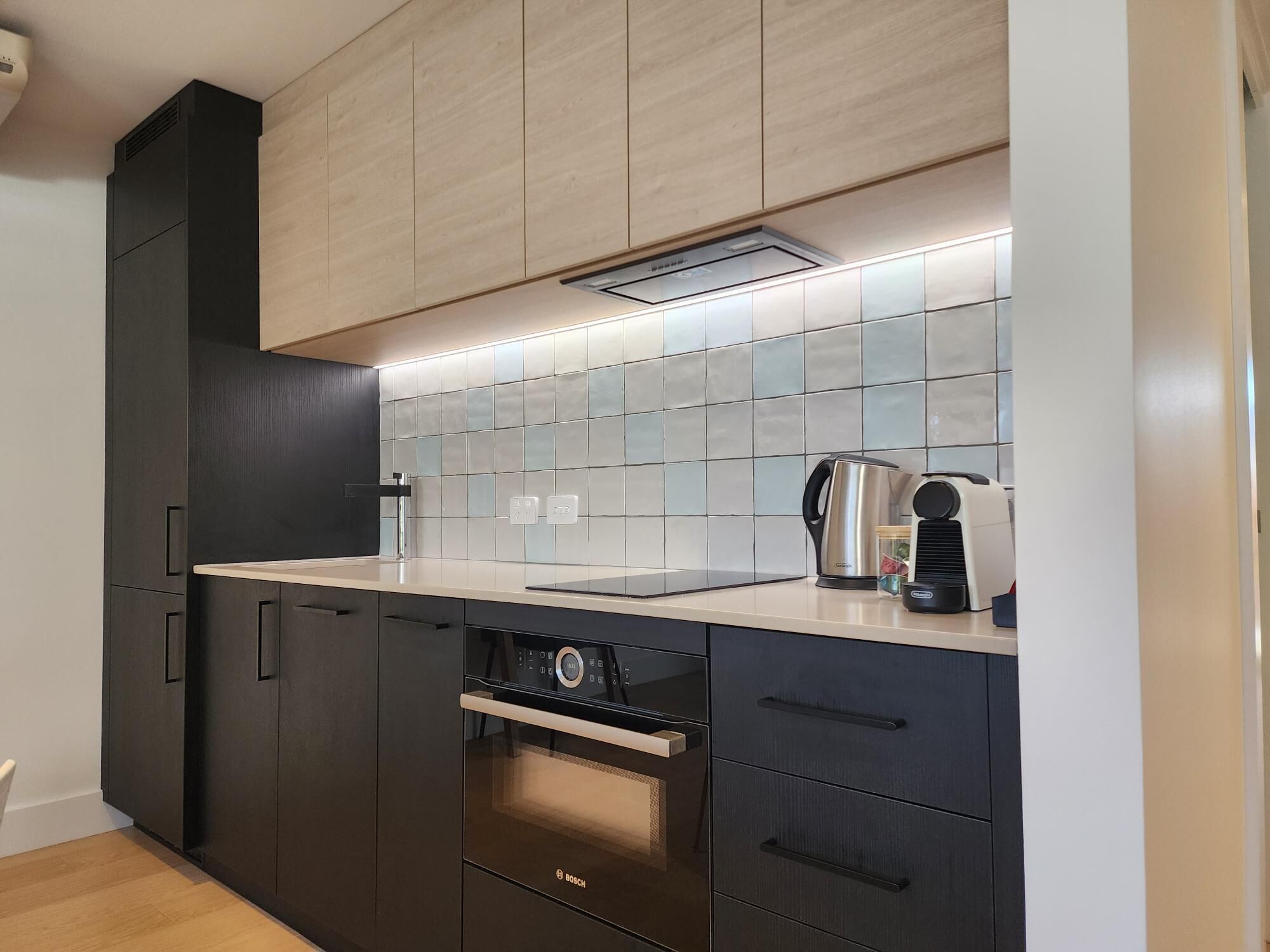 Eine moderne Küche mit dunklen Schränken, einem Bosch-Backofen, einer Kaffeemaschine und einer gefliesten Spritzschutzwand.