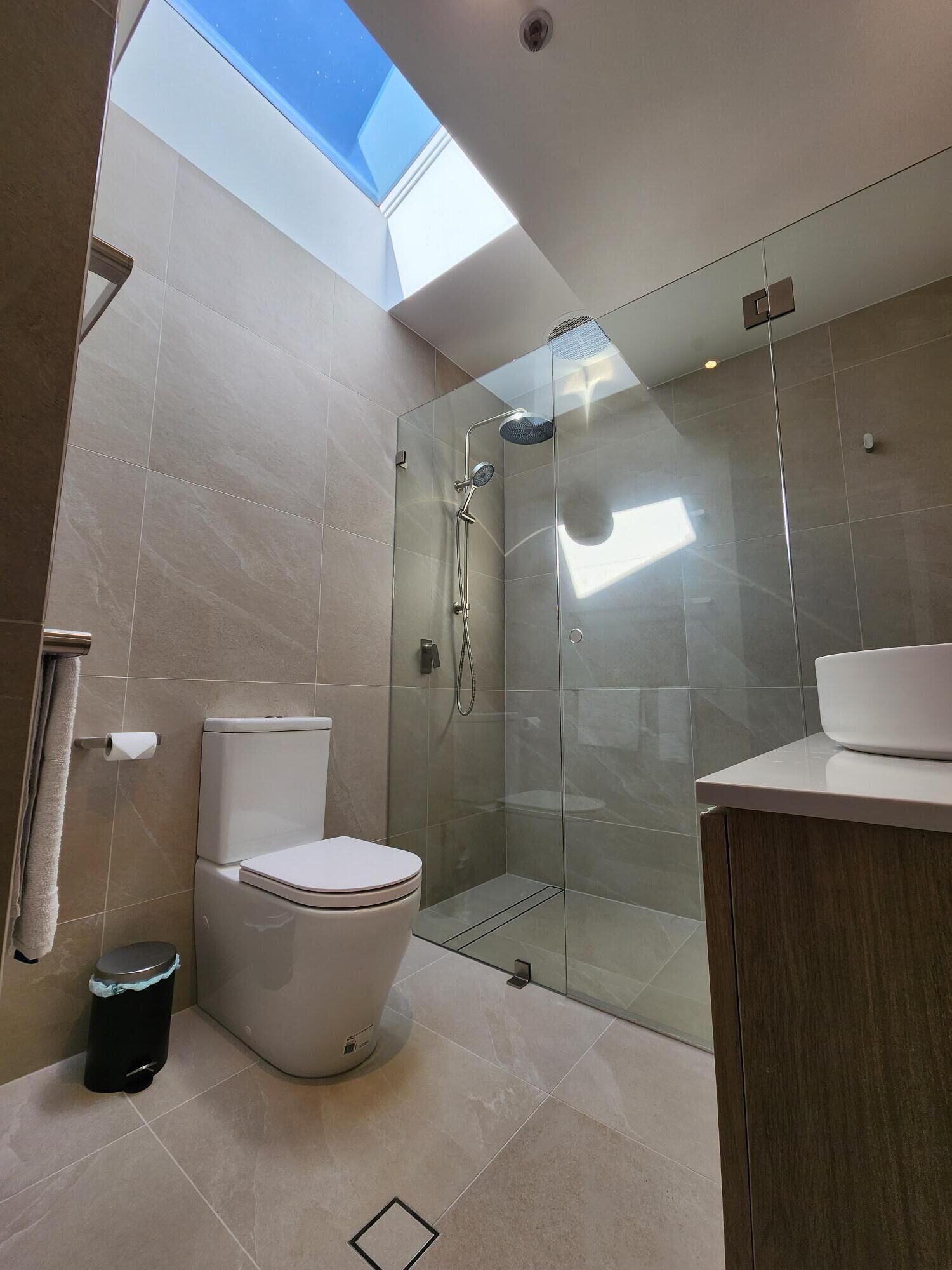 Un baño moderno con tragaluz, ducha envuelta en vidrio, inodoro y lavamanos.