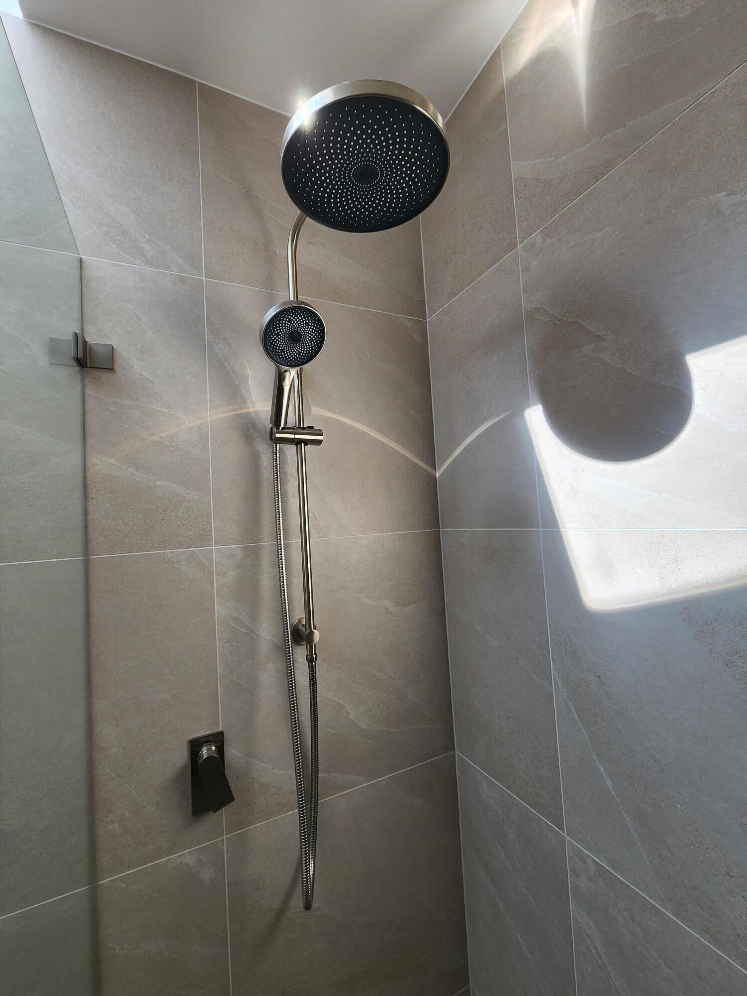 A shower with a roundhead showerhead and a handheld shower attachment.